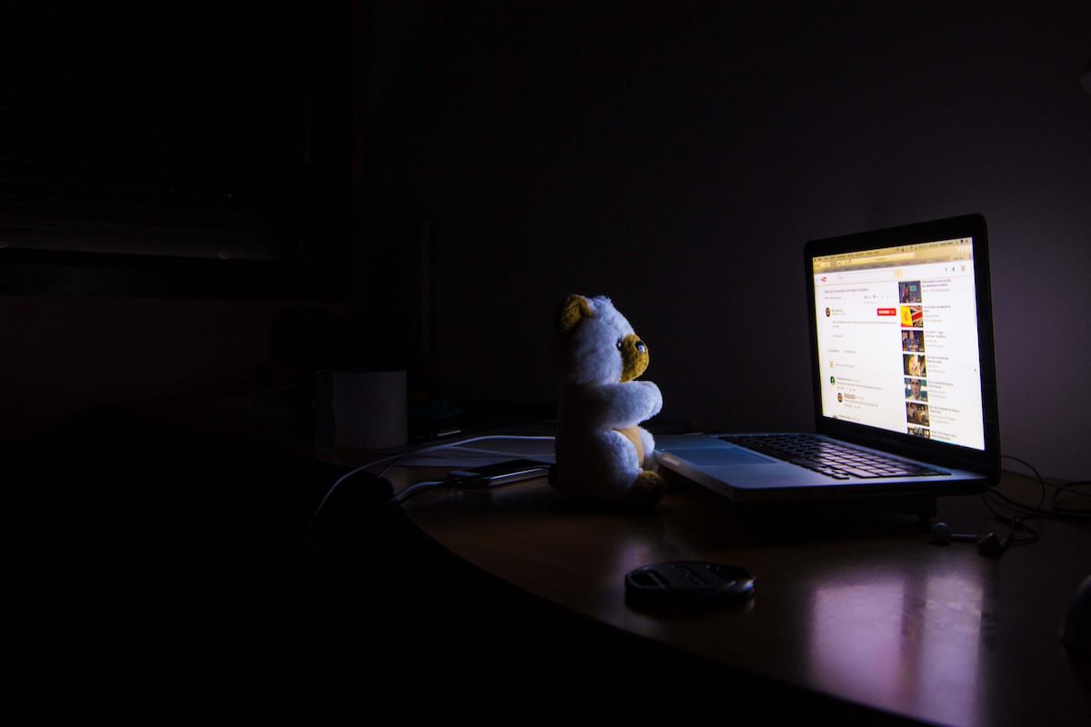 暗闇の中でパソコンを眺めるクマ人形